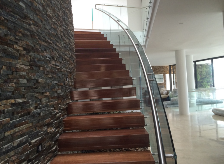 Pasamanos curvo en acero inoxidable en escalera de madera con muro de piedra